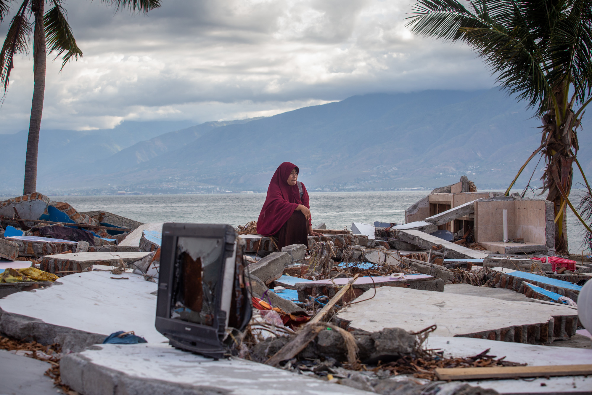 Frau sitzt auf Trümmerhaufen am Strand von Sulawesi, Indonesien.