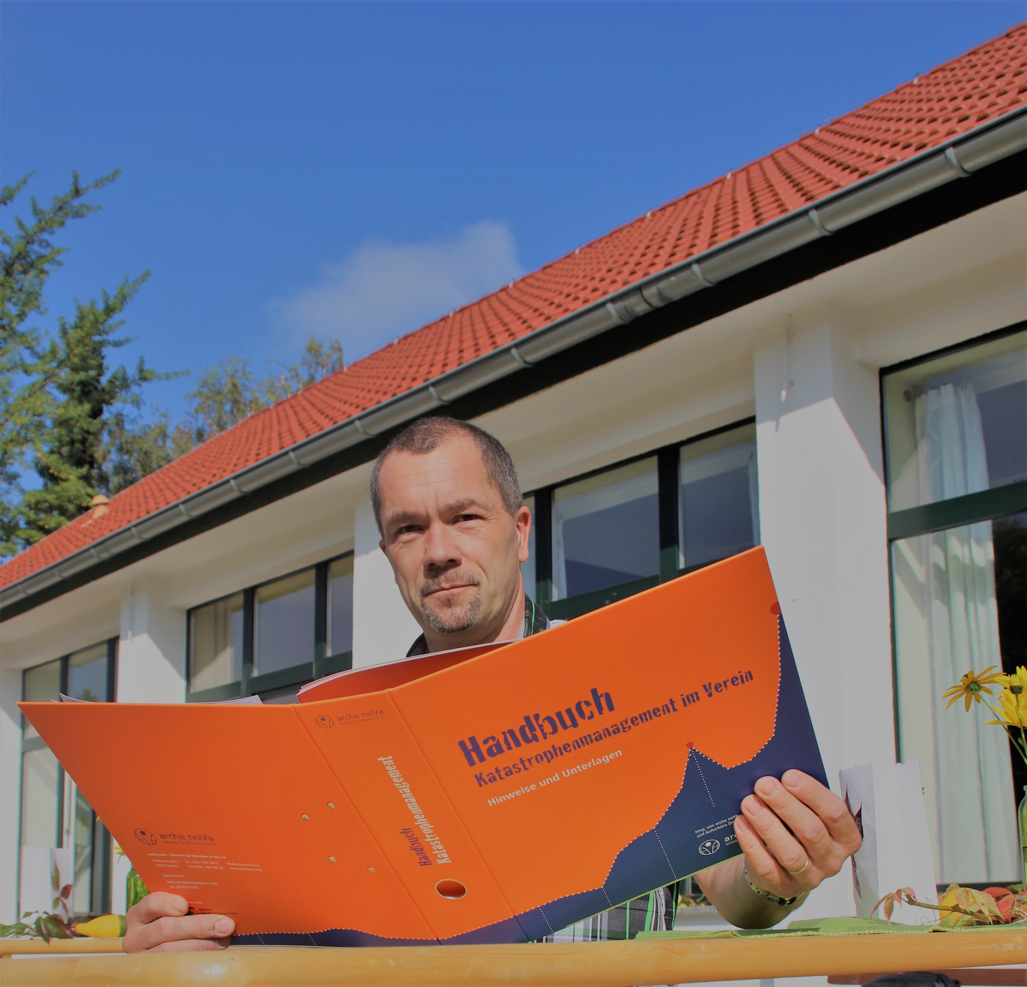 Christoph Wähler hält einenen orangen Aktenordner in der Hand, mit der Aufschirft Handbuch Katastrophenmanagement.